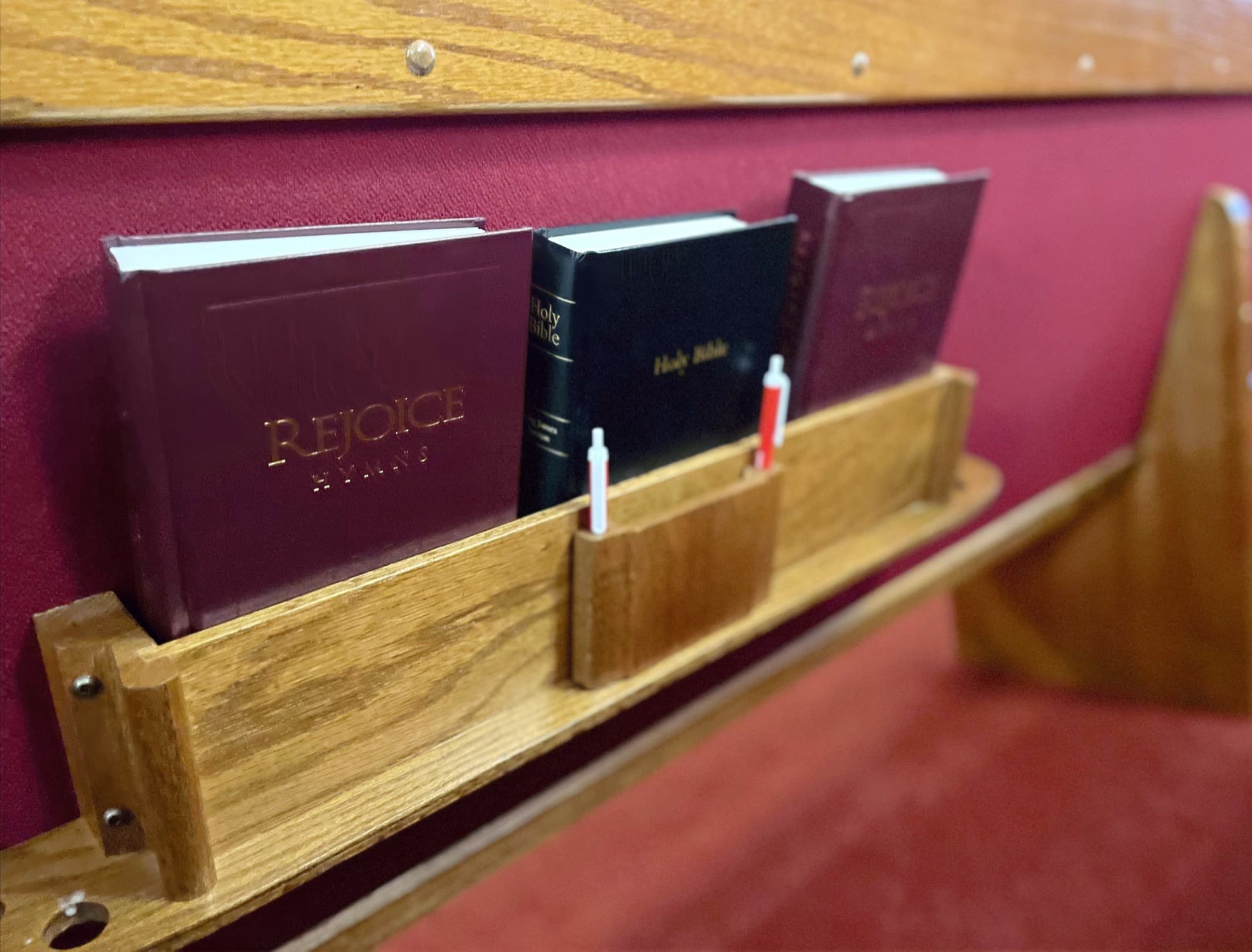 Rejoice hymnals and a Holy Bible in an oak pew rack at Blissfield Baptist Church